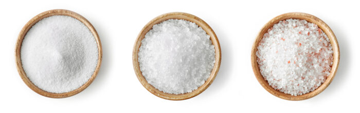 Top view of three wooden bowls of salt to varying degrees of coarseness, with the finest at the left and the least at the right.