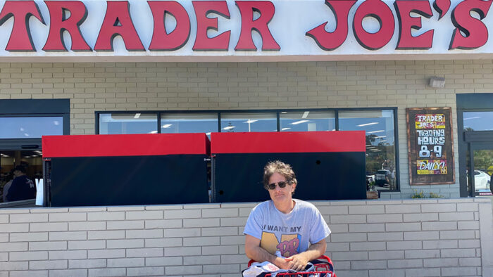 Author leaning on a shopping cart under a Trader Joe's sign.