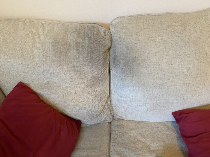 A stain the exact size of the author's head on his beige couch in between cushions and two red pillows.