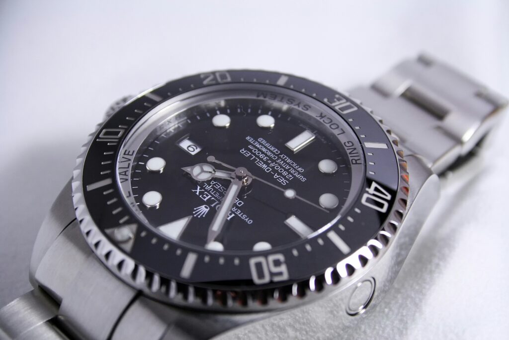 Rolex Submariner stainless steel watch with black dial and rotating bezel resting on a white surface in soft natural light, casting reflective highlights and shadows across the bracelet and face.