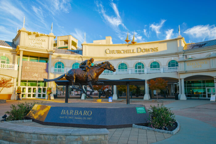 Bronze horse and jockey statue in front of the Churchill Downs entrance, with the venue’s name displayed prominently above.