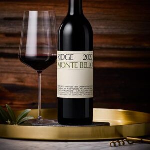 Bottle of Ridge Monte Bello 2022 Cabernet Sauvignon beside a filled wine glass on a gold tray.