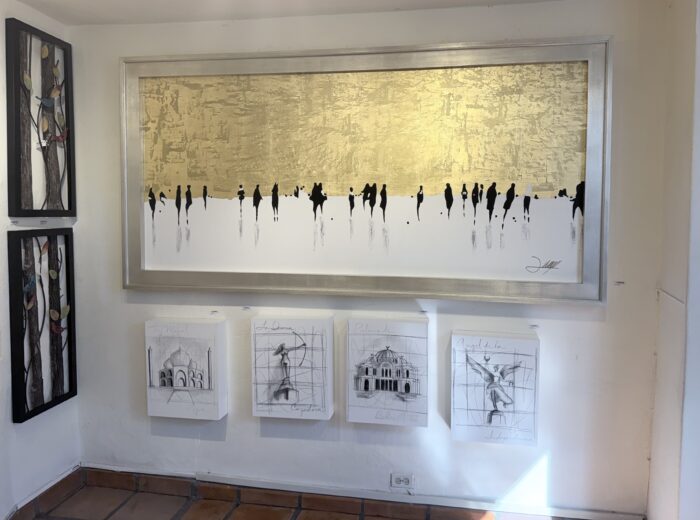 Large abstract artwork with gold and white tones above a row of architectural sketches displayed in a gallery setting.