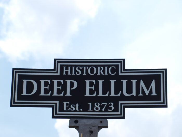 Historic Deep Ellum sign reading “Est. 1873” against a bright blue sky with soft clouds, marking the entrance to the iconic Dallas entertainment district.