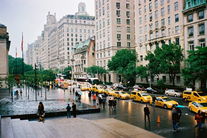 Busy New York City street with yellow taxis and pedestrians on a rainy day, framed by tall buildings near Central Park.