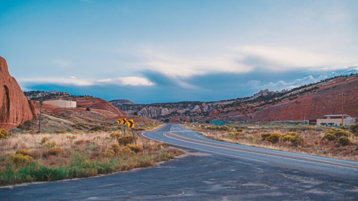 A winding desert highway cuts through the red rock landscape near Route 66 in the American Southwest. The empty road, expansive sky, and rugged terrain capture the isolation, freedom, and mythology long associated with the open road.
