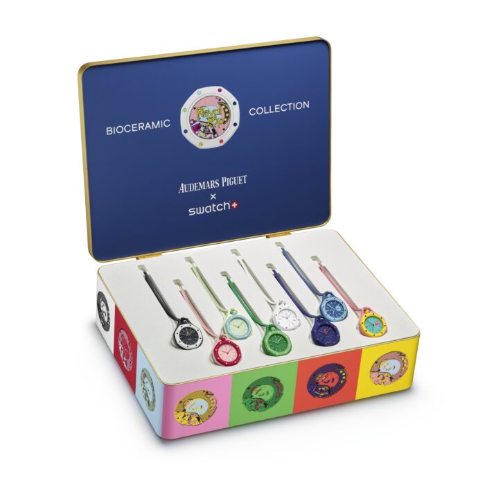 Open presentation case displaying the Audemars Piguet x Swatch Bioceramic Royal Pop collection featuring seven colorful watches arranged in a white-lined display box. The blue case lid is branded with “Bioceramic Collection” and the AP x Swatch logos, while the exterior features bold pop-art inspired graphics in bright pink, green, yellow, and orange tones.
