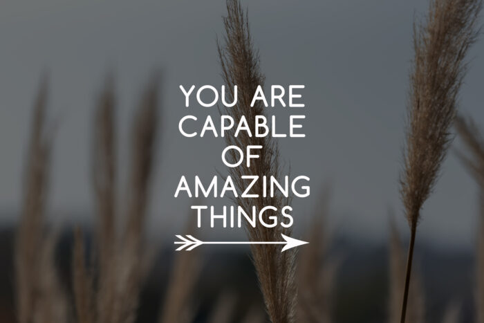 Inspirational text reading “You Are Capable of Amazing Things” appears in white lettering over a softly blurred background of tall ornamental grasses. A simple arrow graphic sits beneath the message, reinforcing themes of motivation, growth, confidence, and personal achievement.