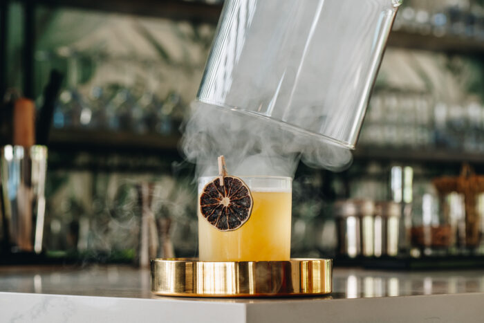 Smoky, garnished cocktail. A bartender prepares a cocktail with smoke effect and dried fruit garnish at a lively bar during the evening.