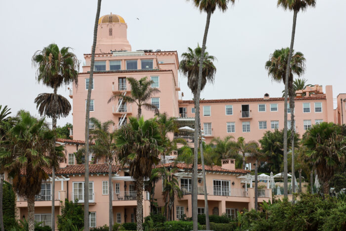 Exterior view of the historic La Valencia Hotel in La Jolla, California, showcasing its iconic blush-pink Spanish-style architecture, signature domed tower, and lush palm trees overlooking the Pacific coastline.