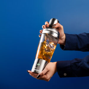 amber liquid and ice against a bold cobalt blue background, highlighting the drink-mixing process.