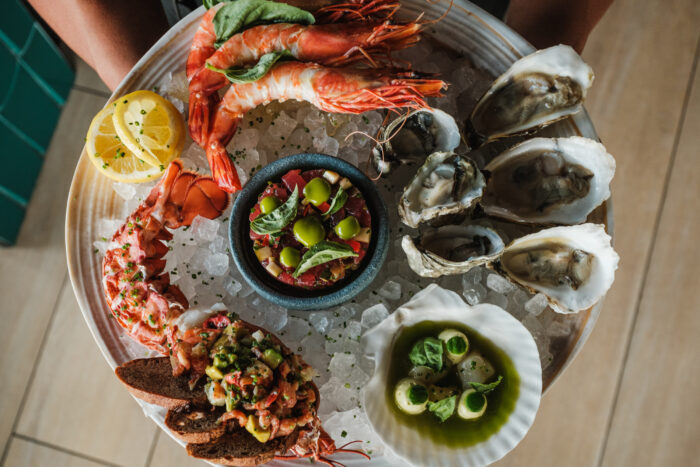 An abundant seafood tower served over crushed ice with oysters, shrimp, lobster, crudo, shellfish, citrus, herbs, and toasted bread, presented as a signature Bar Boheme brunch offering.