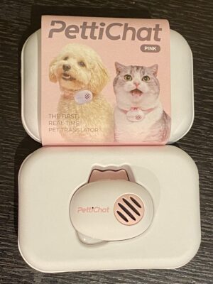 PetiChat pet translator device resting on its charging case next to the product packaging featuring a dog and cat wearing the device.
