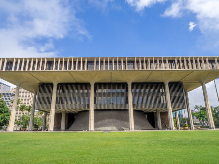 Hawaii State Capitol in Honolulu featuring its distinctive open-air modernist design, columned exterior and broad lawn beneath a blue sky.