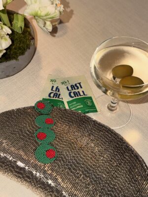 Last Call after-alcohol wellness supplement packets beside a cocktail with olives and a beaded clutch on a table.