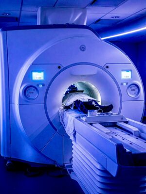 Patient undergoing a full-body MRI scan inside a large medical imaging machine illuminated by blue light.