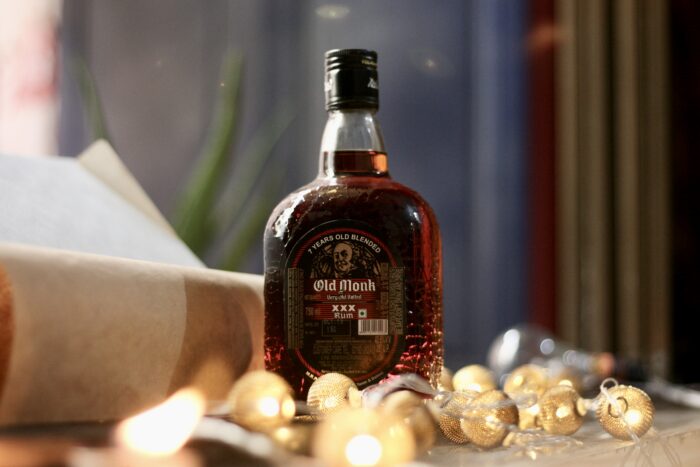 Bottle of Old Monk XXX Rum displayed beside a window, surrounded by warm decorative string lights.