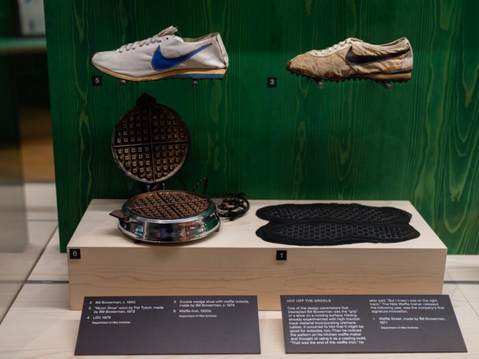 Early Nike running shoes displayed with a waffle iron and waffle sole, illustrating the origins of Nike’s waffle sole design.
