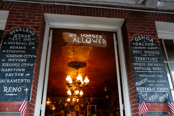Entrance to the historic Genoa Saloon, with hand-painted signs, American flags and warm vintage lighting visible inside.