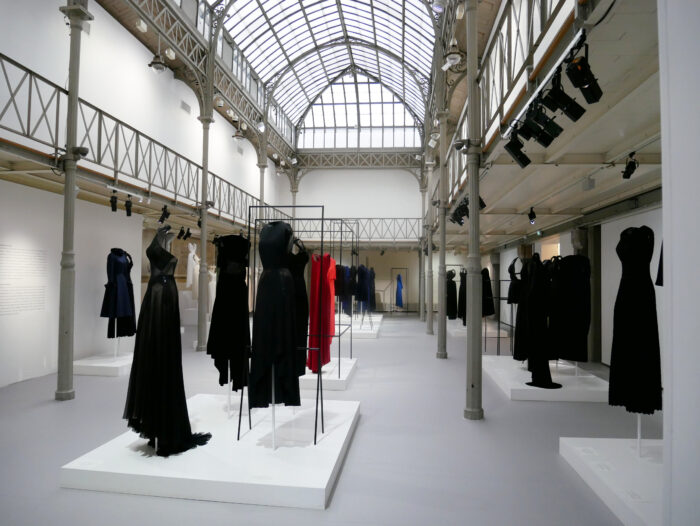Paris fashion exhibition featuring black, white, blue and red dresses displayed in a glass-roofed gallery.