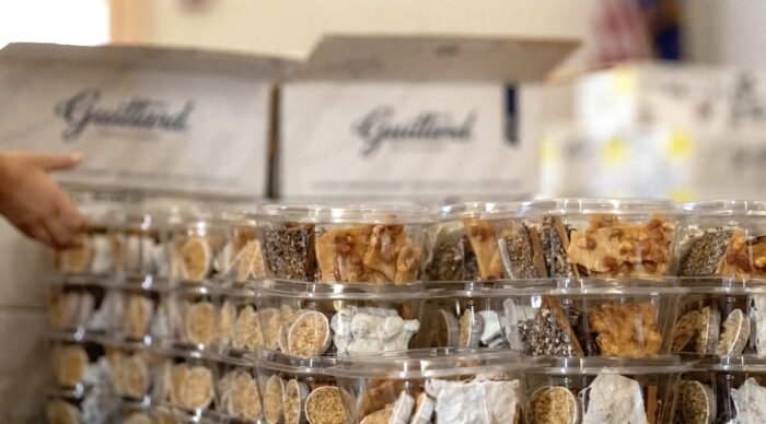 Assorted handmade candies and confections are packaged in clear containers, with Genoa-branded boxes in the background.