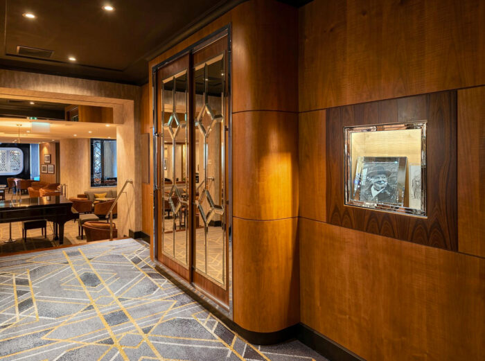 Wood-paneled corridor at the American Bar at The Savoy, featuring mirrored Art Deco doors, geometric carpeting and a framed historic photograph.